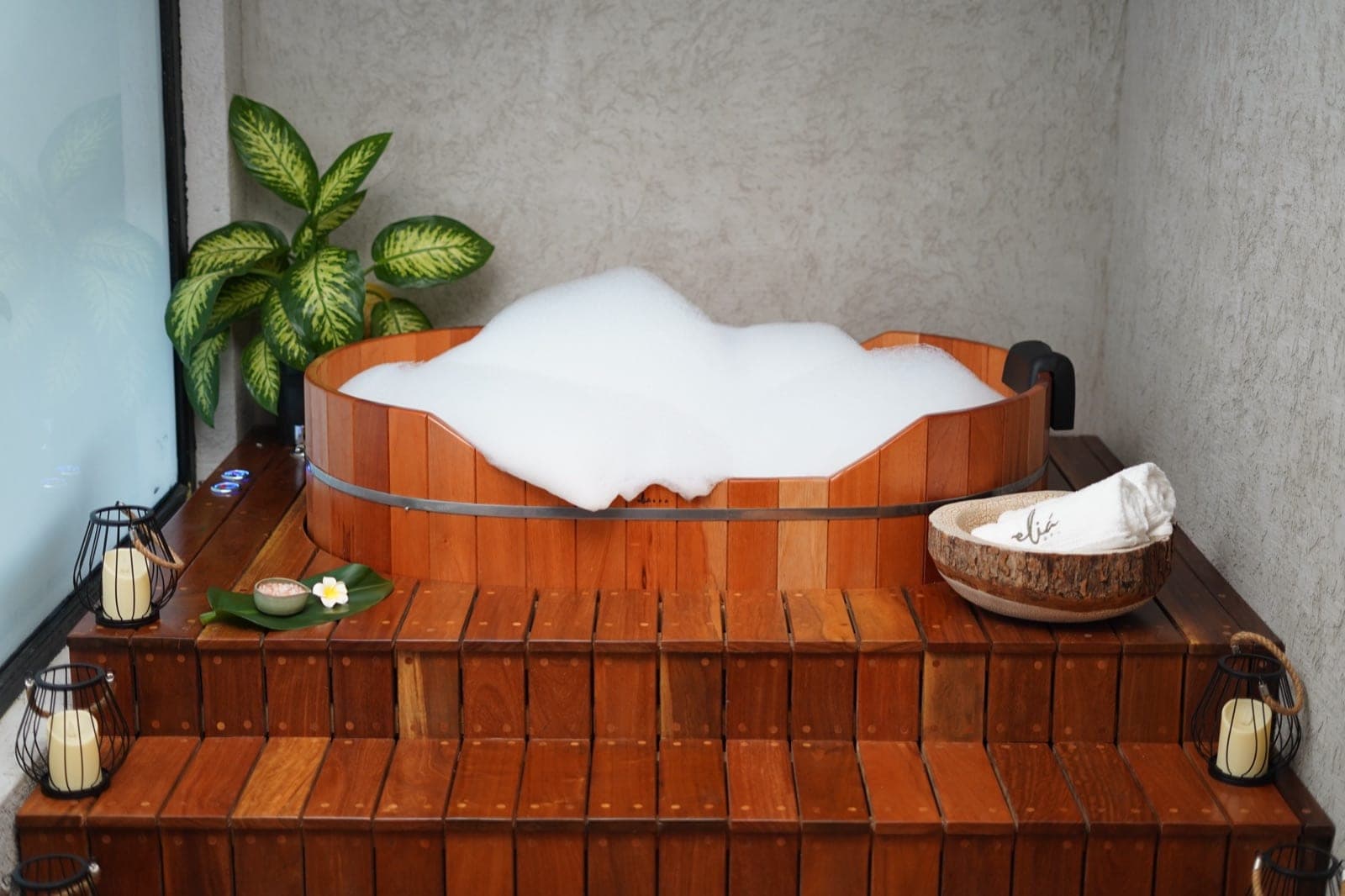 Ofurô de madeira preparado com espuma, ao lado de folhagem